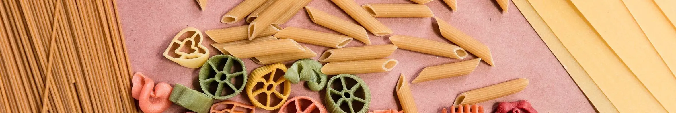 Verschillende pasta soorten op een roze achtergrond. Penne, spagethi, lasagne vellen
