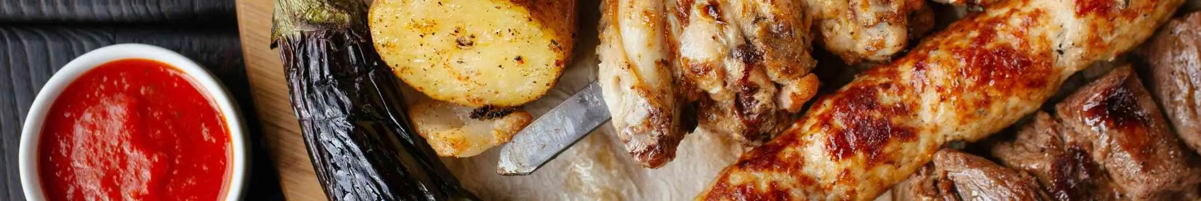 Tafel vol met gebarbecuede kip, geroosterde paprika, gegrilde aardappelen en sausjes. 