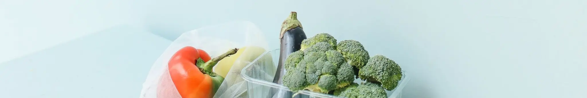 Verse groenten zoals paprika, broccoli en aubergine op een gekleurde achtergrond.