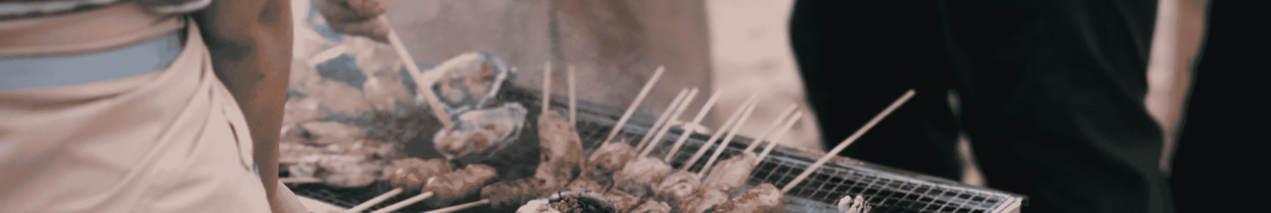 Iemand die aan het barbecuen is en vrienden die er gezellig om heen staan. Tips voor goedkoop en lekker barbecueën